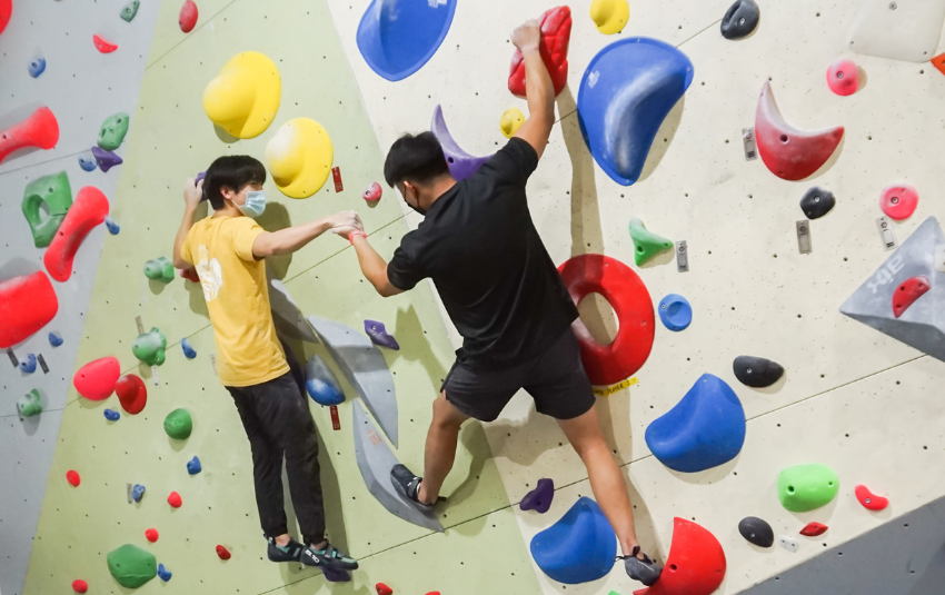 Instructor helping man on bouldering wall at Fit Bloc