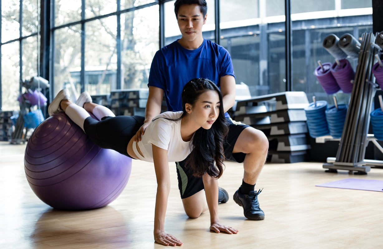 asian-woman-playing-yoga-by-yoga-ball-with-trainer-2021-09-02-14-56-29-utc